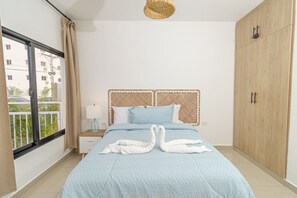 Un dormitorio con cama, mesita de noche, lámpara, armario y vistas a edificios.