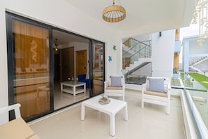 Un espace de vie extérieur moderne, doté d’une porte vitrée donnant sur un balcon, de meubles blancs et d’un escalier visible au fond.
