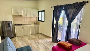 A compact room with a kitchenette, a sofa, a bed, and a balcony with curtains.