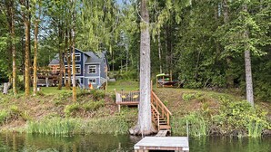 A lakeside cabin with a dock, surrounded by trees and a deck. - Lakefront-Hot Tub, 2 Kitchens, Kayaks, Game Room (Bremerton)
