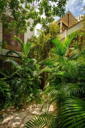 A lush garden with dense foliage and a building with wooden slats and a balcony.