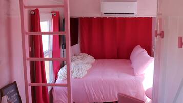 Een kamer in roze tinten met een stapelbed, een raam met rode gordijnen en een airconditioning.