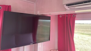 Um interior em tons de rosa, com televisão de tela plana na parede, cortinas cor-de-rosa e aparelho de ar condicionado.