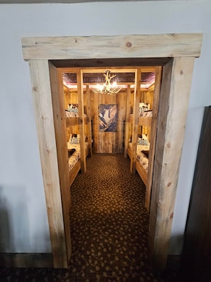 Een smalle gang met houten wanden en een kamer met een kroonluchter en een ingelijst kunstwerk aan de muur, met een patroon vloer.