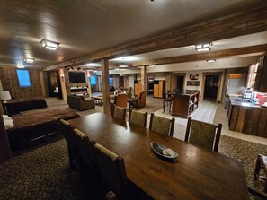 Un'ampia stanza con un grande tavolo da pranzo in legno, diverse disposizioni di posti a sedere, un camino e un angolo cottura.