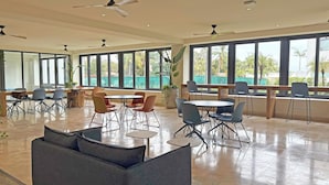 A spacious indoor area with multiple seating arrangements, large windows, and ceiling fans. - Modern Studio with Ocean View (Cruz de Huanacaxtle)