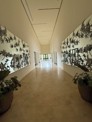 A hallway with a long corridor, walls adorned with dinosaur sculptures, and potted plants at the ends.