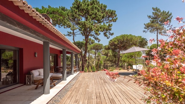 Une terrasse en bois avec des sièges extérieurs, un bâtiment rouge et des arbres environnants.