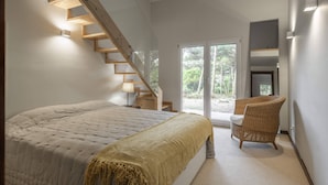 Une chambre avec un grand lit, un escalier en bois, une chaise et une vue sur l’extérieur.