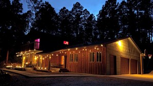 A wooden cabin with a porch, string lights, and a basketball hoop.