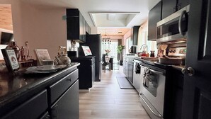 A modern kitchen with black cabinetry, stainless steel appliances, and a wooden floor.