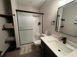 Ein modernes Badezimmer mit einer Duschkabine aus Glas, einer weißen Toilette, einem Waschbecken mit Marmorplatte und einem großen Spiegel.