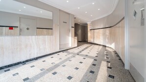A hotel corridor with a tiled floor, a mirrored wall, and a door with a sign. - L'Antibes - Climatisation - Pet friendly (Antibes)