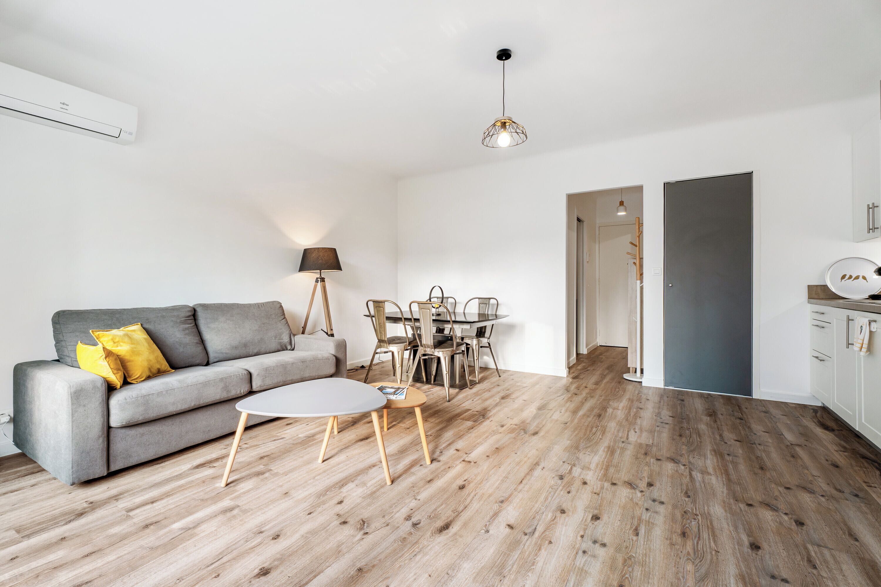 A modern living room with a grey sofa, a round coffee table, and a dining area with a table and chairs.