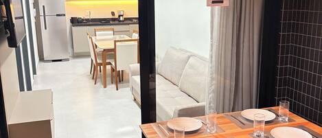 Una cocina moderna con armarios blancos, un refrigerador de acero inoxidable y un comedor con una mesa de madera para cuatro.