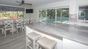 A modern kitchen with a marble countertop, white cabinetry, and a large window overlooking a pool. - Tranquil OASIS (Sarasota)