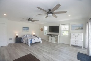 A bedroom with a bed, two ceiling fans, a TV, a dresser, and a window.