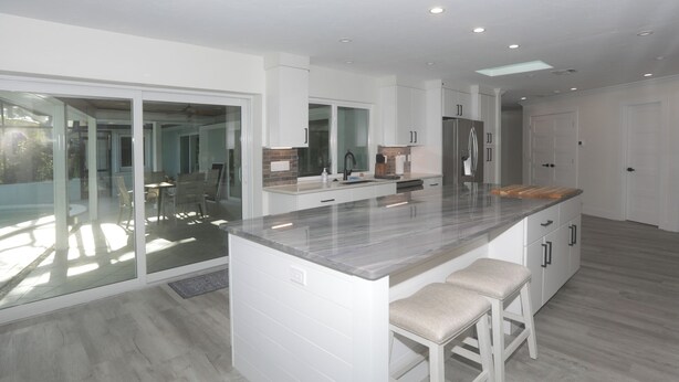A modern kitchen with a large island, white cabinetry, and a glass door leading to a balcony. - Tranquil OASIS (Sarasota)