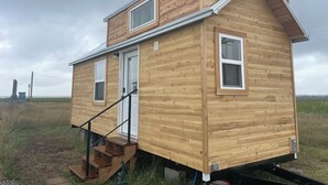 A wooden cabin with a front door, two windows, and a staircase leading to the entrance.