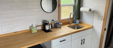 Cocina compacta con mostrador de madera, un lavamanos, una cafetera y un espejo.