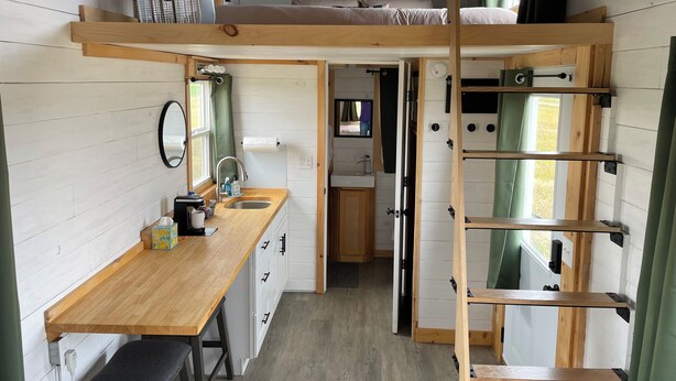 A compact, well-organized cabin with a bunk bed, a kitchenette, a small bathroom, and a wooden desk.