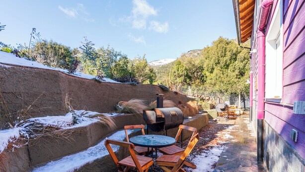 An outdoor seating area with a round table and wooden chairs, a barbecue grill, and a stone wall.