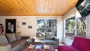 A living room with a wooden ceiling, a red sofa, a grey sofa, and a coffee table with books and a remote control.
