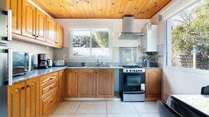 A modern kitchen with wooden cabinets, a stainless steel stove, and a large window providing a view of the outdoors.