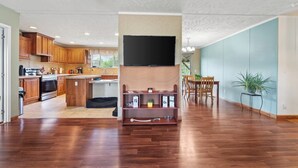 A spacious living area with a kitchen, dining table, and a flat-screen TV mounted on a wall. - 3BR Home Near Snowshoe | Tesla | Pet Friendly  | Elk Mountain Apres’ (Marlinton)