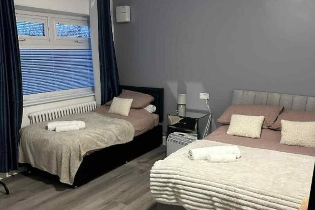 Ein Hotelzimmer mit zwei Betten, einem Heizkörper, einem Nachttisch, einer Lampe und einem Fenster mit Vorhängen.