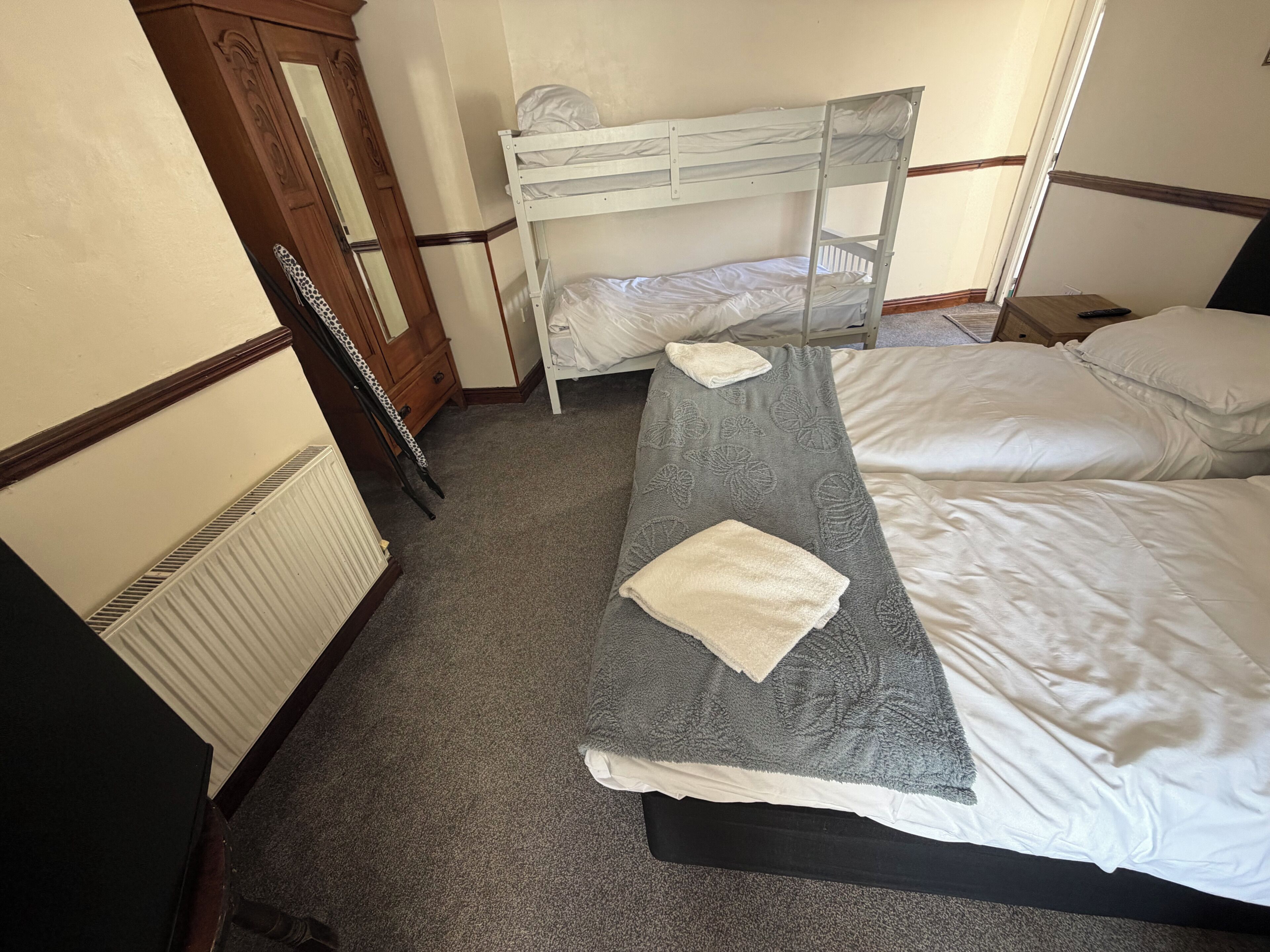 A bedroom with a bunk bed, a single bed, a wooden dresser, and a radiator.