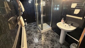 A bathroom with a glass shower enclosure, a sink, and a mirror with lights. - OYO Prince of Wales Country Hotel (Princetown)