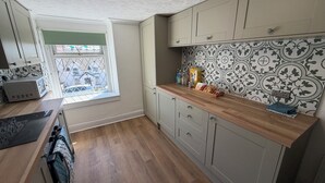 A kitchen with a window, wooden cabinets, a microwave, and a tiled backsplash. - OYO Prince of Wales Country Hotel (Princetown)