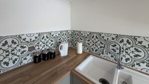 A kitchen with a wooden countertop, a sink, and patterned backsplash tiles. - OYO Prince of Wales Country Hotel (Princetown)