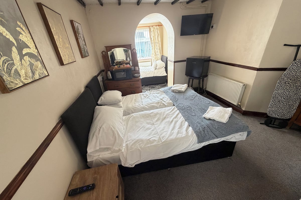 Ein Hotelzimmer mit Bett, Fernseher, Spiegel, Kommode und einem Fenster mit Vorhängen.