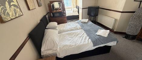 Habitación de hotel con cama, televisión, espejo, cómoda y ventana con cortinas.