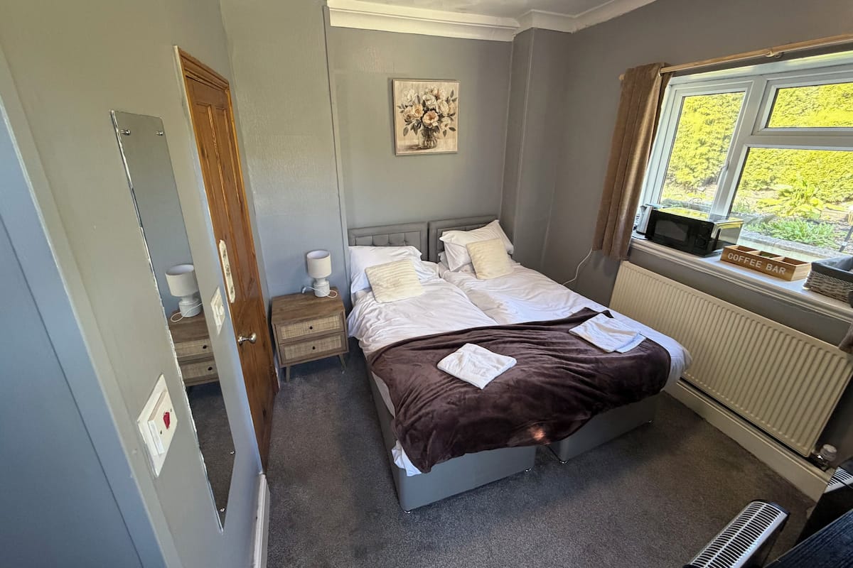 Ein Schlafzimmer mit Bett, Nachttisch, Lampe, Bild, Fenster, Heizkörper und Blick ins Grüne.
