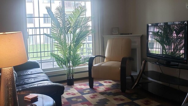 A living room with a sofa, a coffee table, a TV, and a large window with a view of buildings outside. - Downtown Hideaway (Fort McMurray)