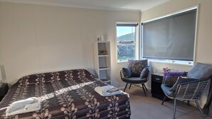 A bedroom with a large bed, a chair, a small table, a shelf, and a window.