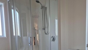 A modern bathroom with a glass-enclosed shower, a white toilet, and a small vanity with drawers.