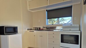 A compact kitchen with white cabinets, a microwave, a stove, and a window with a view of trees.