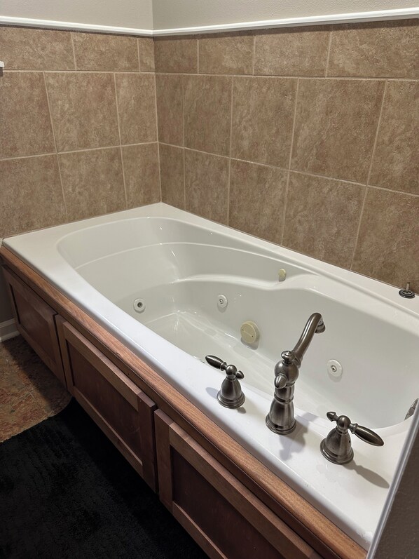 A bathroom with a large white bathtub, wooden vanity, and beige tiled walls.