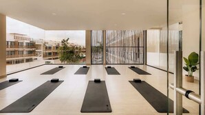A spacious indoor area with exercise mats arranged in rows, large windows, and a view of surrounding buildings. - Makech Samsara Tropical Beach Club Access (Tulum)
