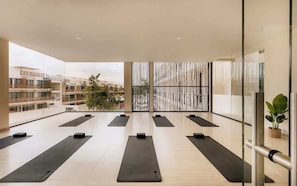 A spacious indoor area with exercise mats arranged in rows, large windows, and a view of surrounding buildings.
