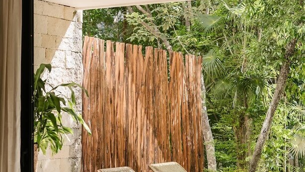 A room with a large window, a wooden table, two lounge chairs, and a woven wall. - Makech Samsara Tropical Beach Club Access (Tulum)
