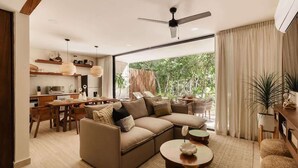 A modern living room with a sectional sofa, dining area, and large windows. - Makech Samsara Tropical Beach Club Access (Tulum)