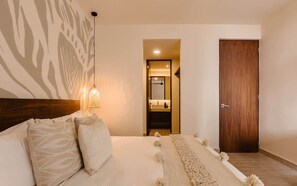 Una camera da letto con un letto, un comodino, un lampadario a sospensione, una porta in legno e un bagno visibile attraverso una porta aperta.