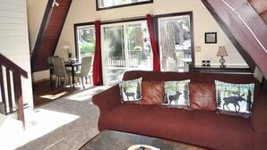 Ein gemütliches Loft-Zimmer mit geneigten Decken, einem kieseligen Couchtisch, einer Ledersofa mit Hirsch-Kissen und großen Fenstern mit Blick ins Freie.