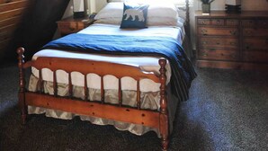 Ein Schlafzimmer mit schrägverdeckter Decke, einem Holzbett, einem Nachttisch, einer Uhr und einem Fenster.