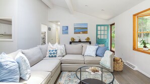 A living room with a beige sectional sofa, a round coffee table, and a view of the outdoors through a window.